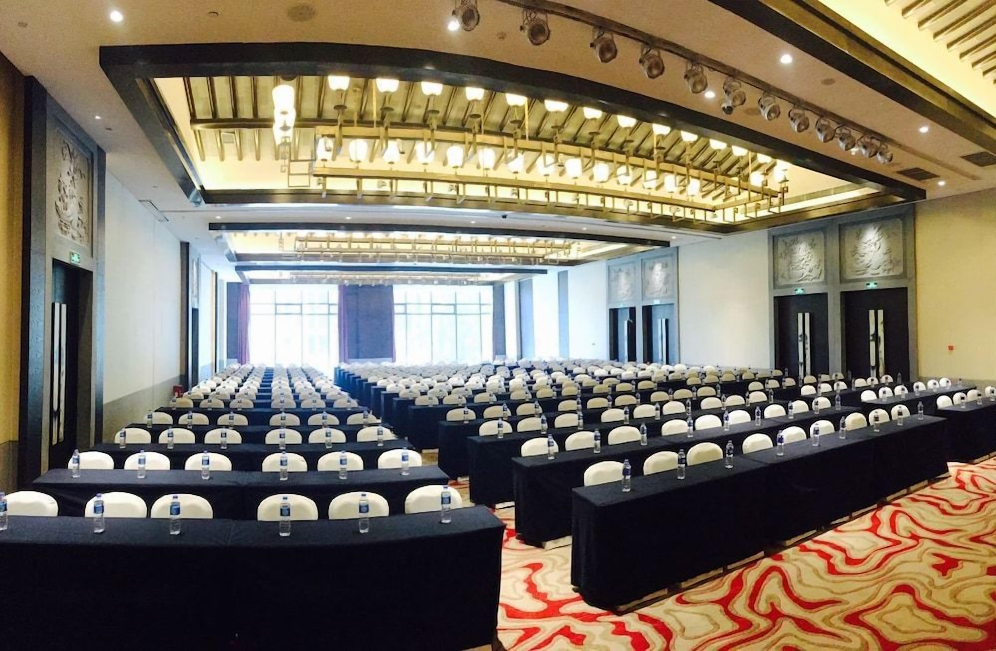 Une salle de conférence avec des rangées de tables et de chaises, une moquette à motifs et un design de plafond moderne.