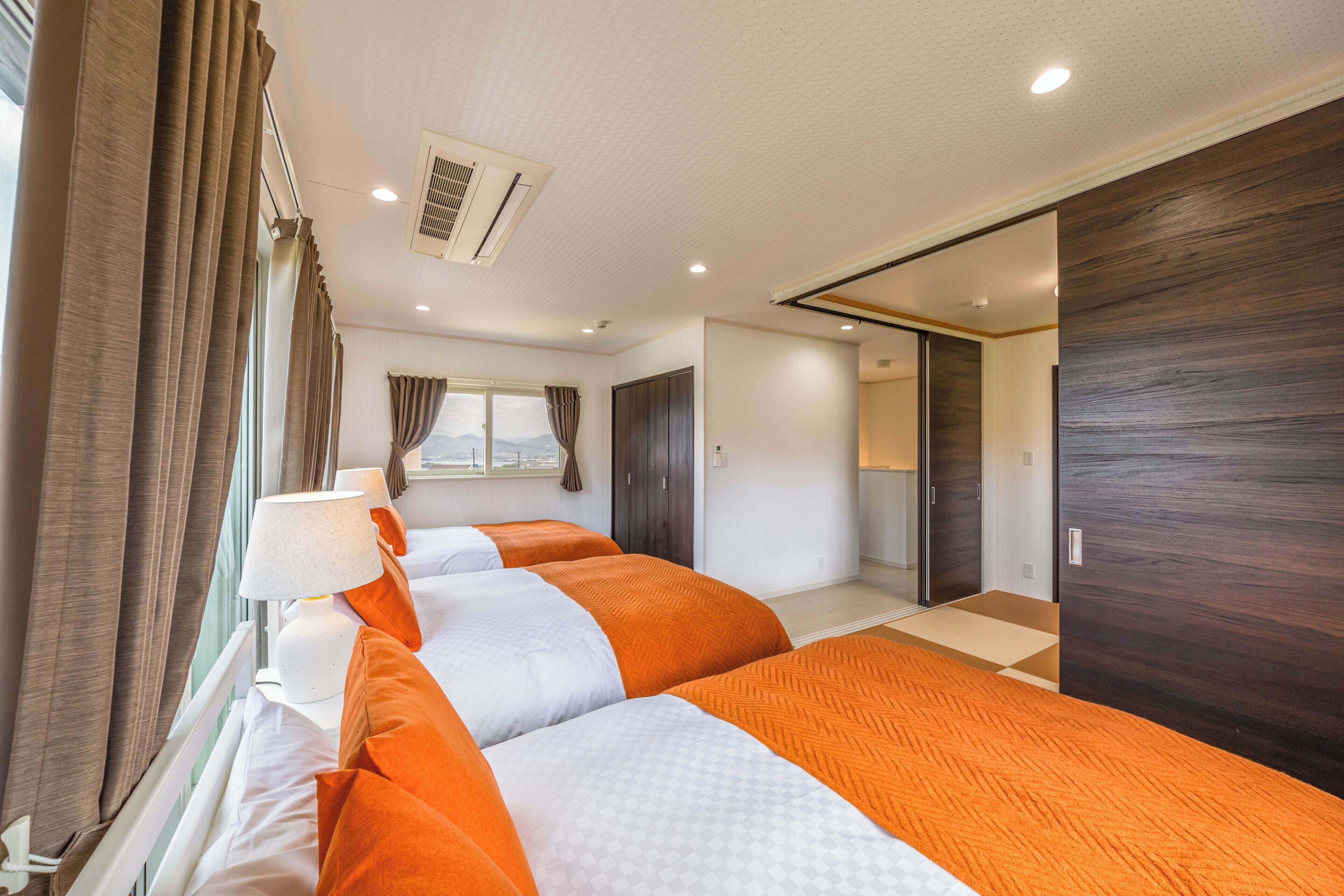 Una habitación de hotel con una cama grande, una ventana con cortinas, un armario y un baño visible a través de una puerta abierta.