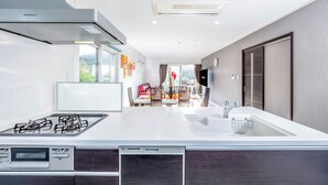 A modern kitchen with a central island, built-in appliances, and a view to a dining area. - Hopehills Hiramatsutei (Shirahama)
