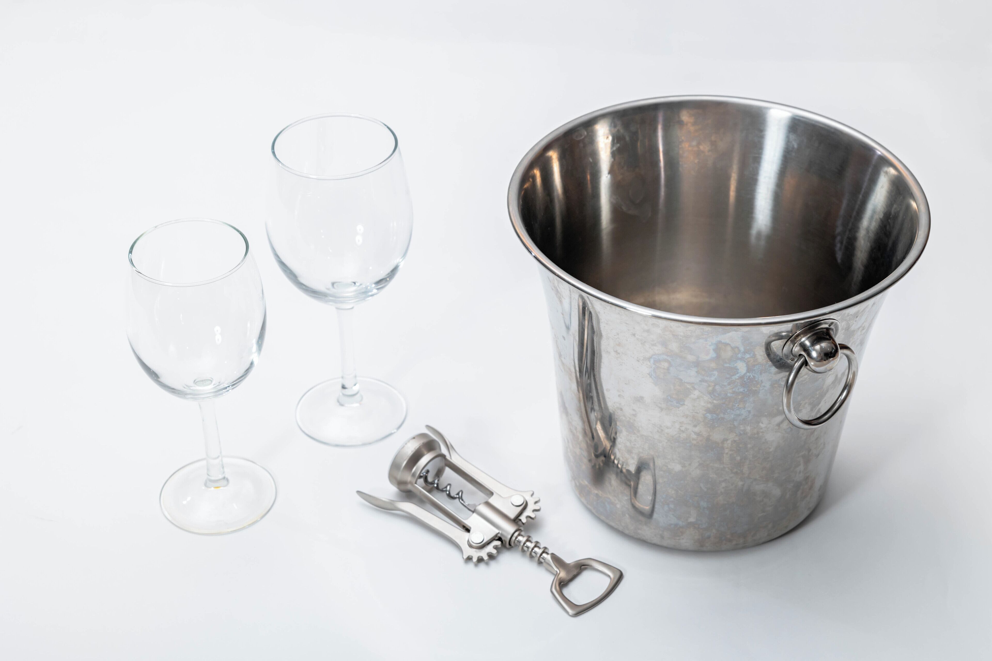 A metallic bucket with a handle and a bottle opener, accompanied by two empty wine glasses.