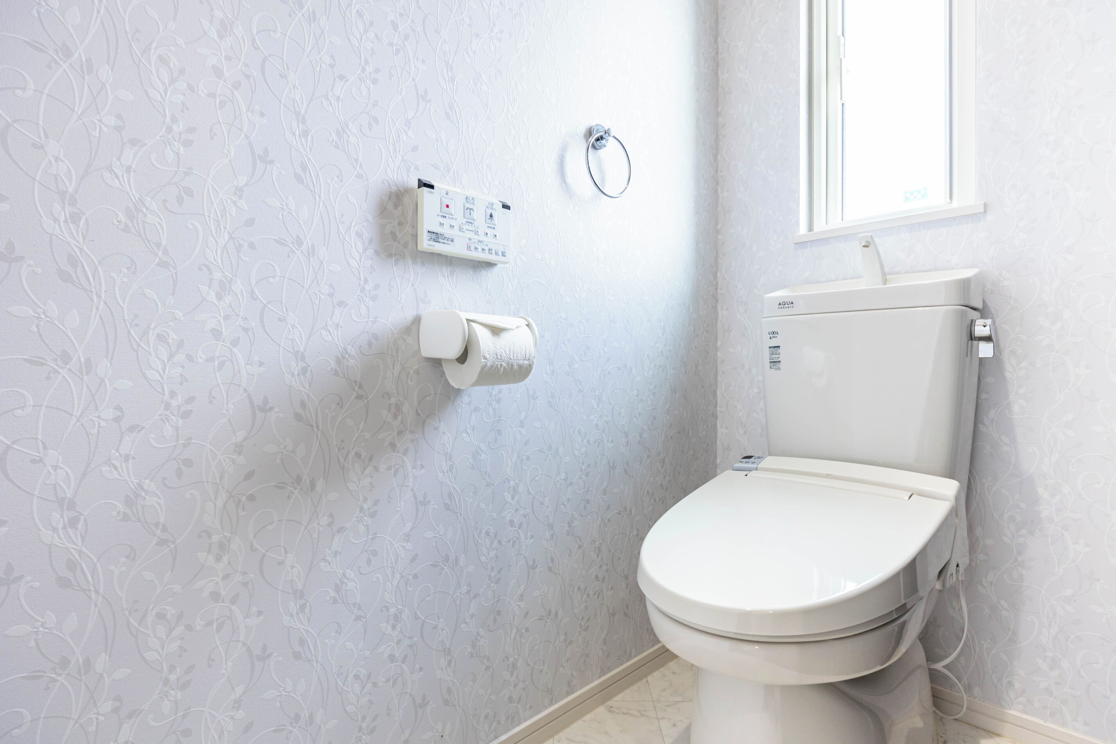A bathroom with a toilet, a toilet paper holder, and a hand sanitizer dispenser on the wall.