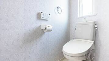 A bathroom with a toilet, a toilet paper holder, and a hand sanitizer dispenser on the wall.