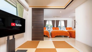 A hotel room with a flat-screen TV, two beds with orange bedding, a checkered floor, and a view of the city through large windows. - Hopehills Hiramatsutei (Shirahama)