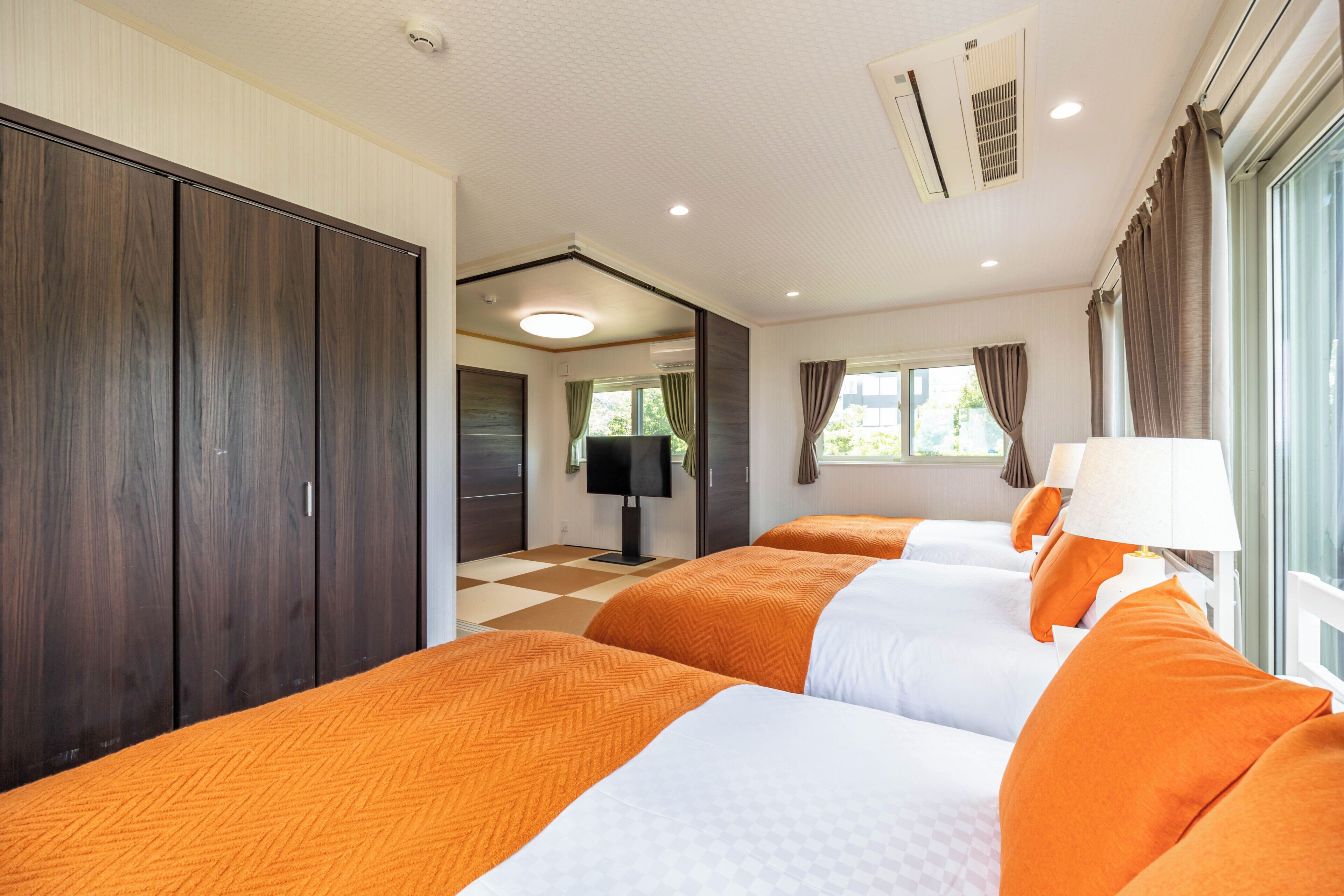 A hotel room with two beds, a large wardrobe, a television, and a window with curtains.