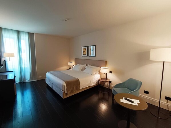 Ein Hotelzimmer mit Bett, Nachttischlampen, einem Sessel, einem kleinen Tisch und einem Schreibtisch mit Lampe.