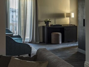 A modern living room with a sofa, a desk with a lamp, and a view through a window with curtains. - Dogana Resort (Molfetta)