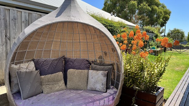 Un espace de détente extérieur circulaire, fait d’un matériau tressé, avec des coussins et un tissu à motifs.