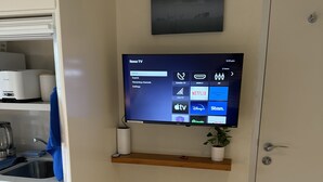 Un salon moderne avec un téléviseur à écran plat fixé au mur, une petite étagère en bois en dessous et une boîte de rangement blanche posée sur le sol.