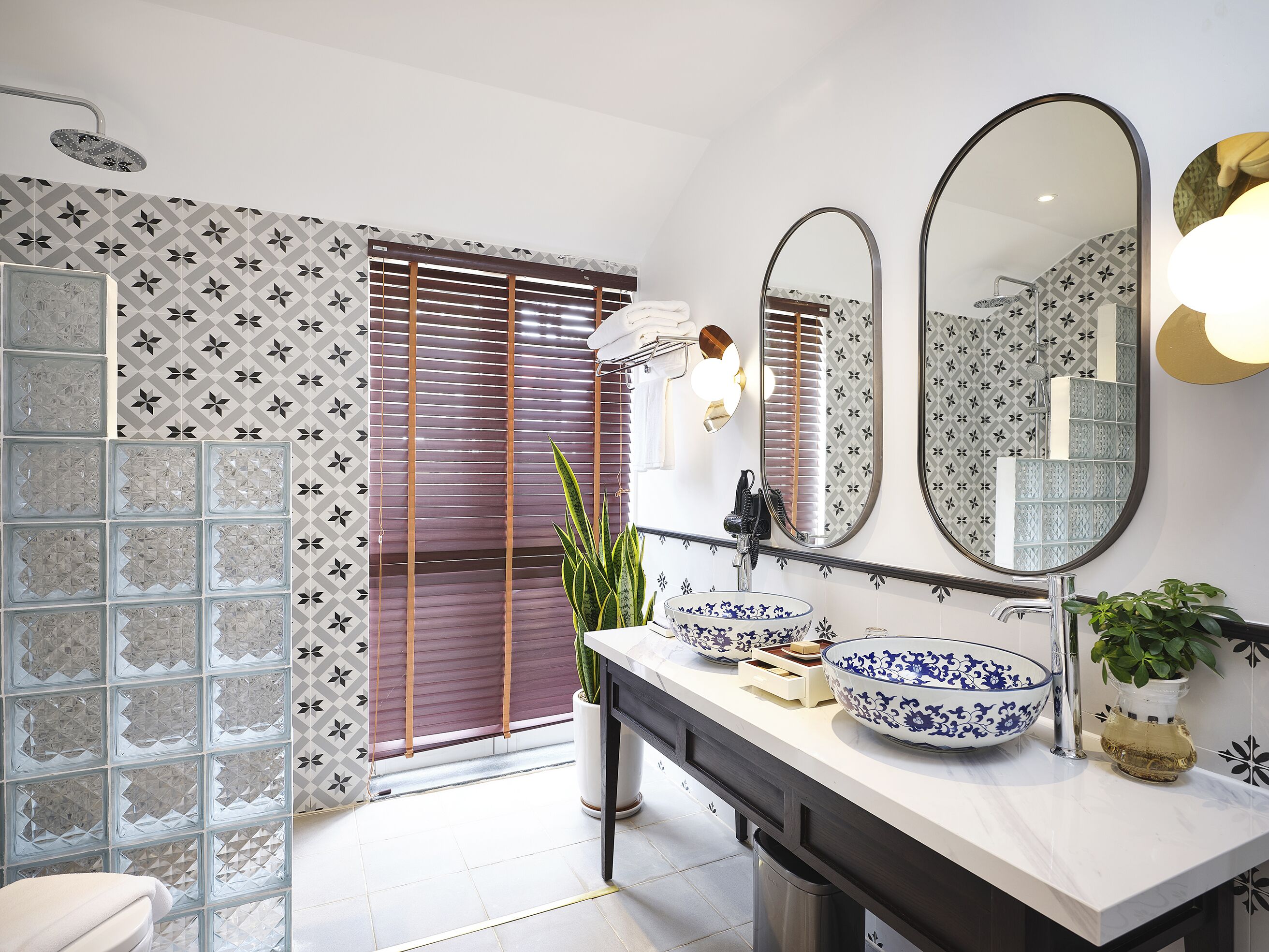 Un baño con ducha, dos espejos, un lavamanos con cuencos decorativos y una planta en maceta.