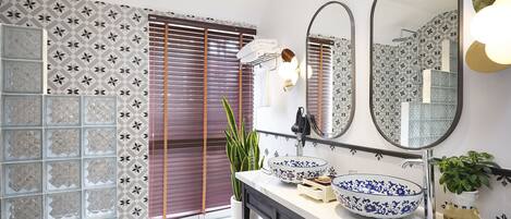 Un baño con ducha, dos espejos, un lavamanos con cuencos decorativos y una planta en maceta.