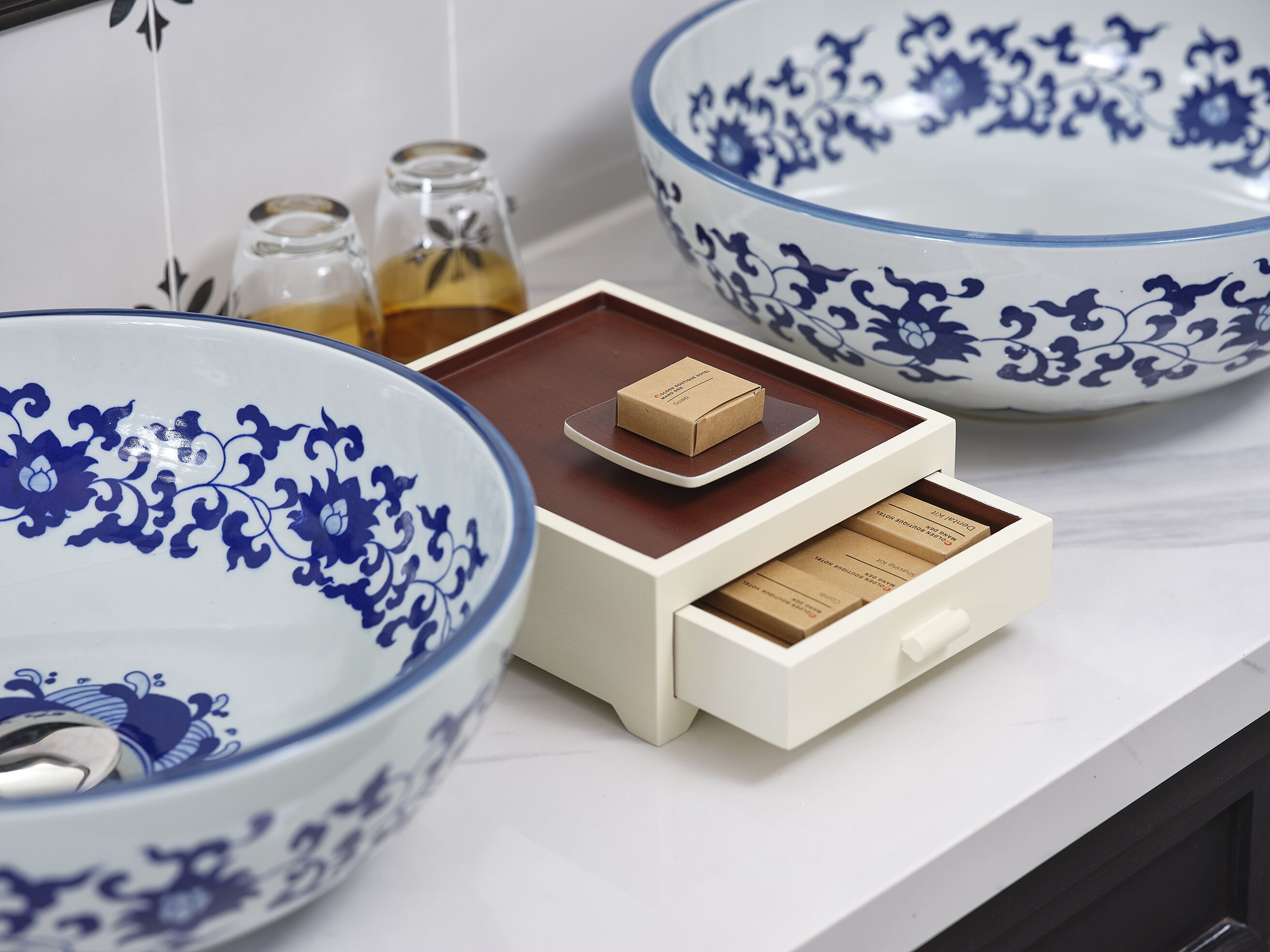 A bathroom with a white sink, a blue and white patterned bowl, and a small wooden tray with a box.