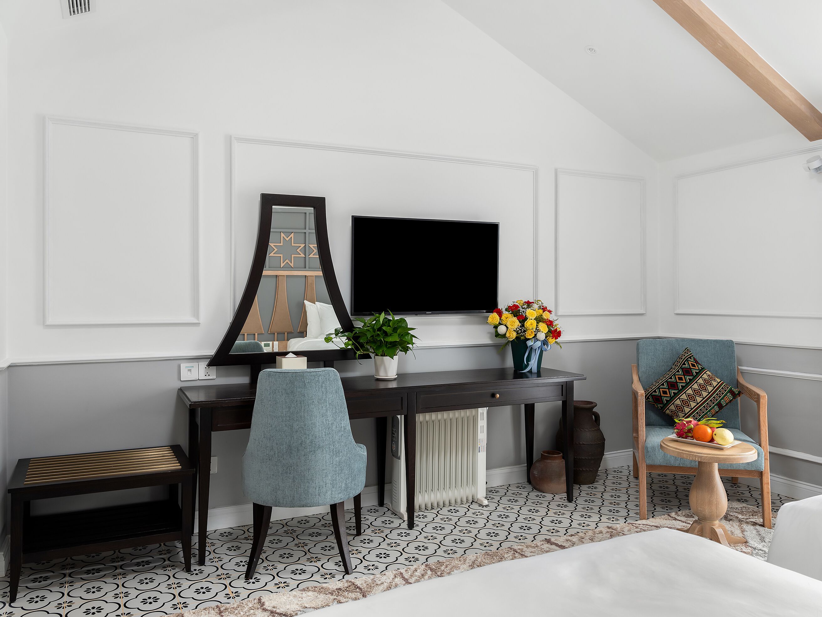 Un dormitorio moderno con cama, escritorio, silla, televisor y un espejo decorativo.