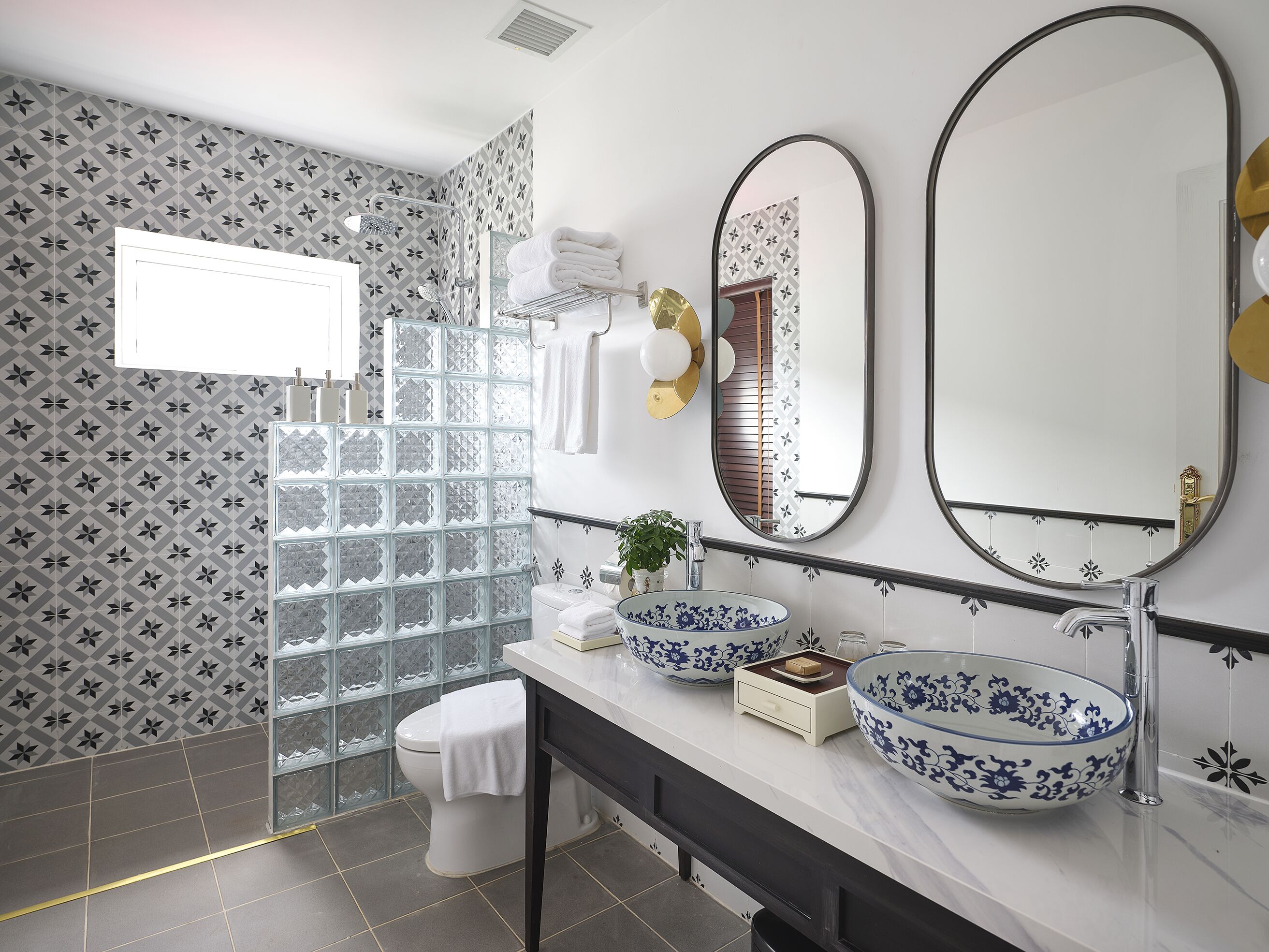 A modern bathroom with a glass shower enclosure, a white toilet, a vanity with two large blue and white patterned bowls, and a large mirror above the vanity.
