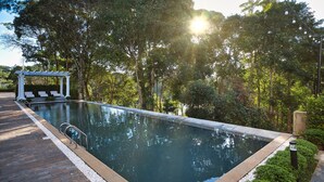 Una piscina rectangular amb terrassa de fusta i una pèrgola amb gandules.