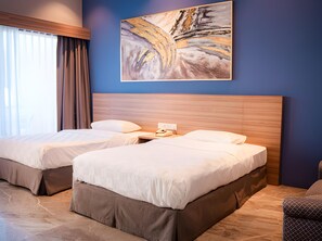 A hotel room with two beds, a wooden headboard, a painting on the wall, and a window with curtains. - Niagara Hotel Lake Toba Resorts (Parapat)