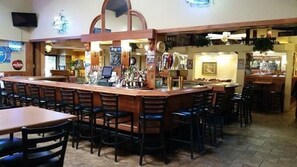 A bar area with a long counter, multiple stools, and a television mounted on the wall. - Americas Best Value Inn Chippewa Falls (Chippewa Falls)