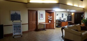 A lobby with a reception desk, a coffee station, a seating area with a sofa, and a poster on the wall.