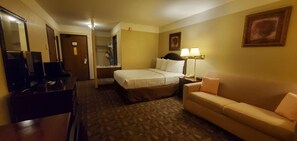 A hotel room with a bed, a sofa, a desk, a mirror, and a lamp.