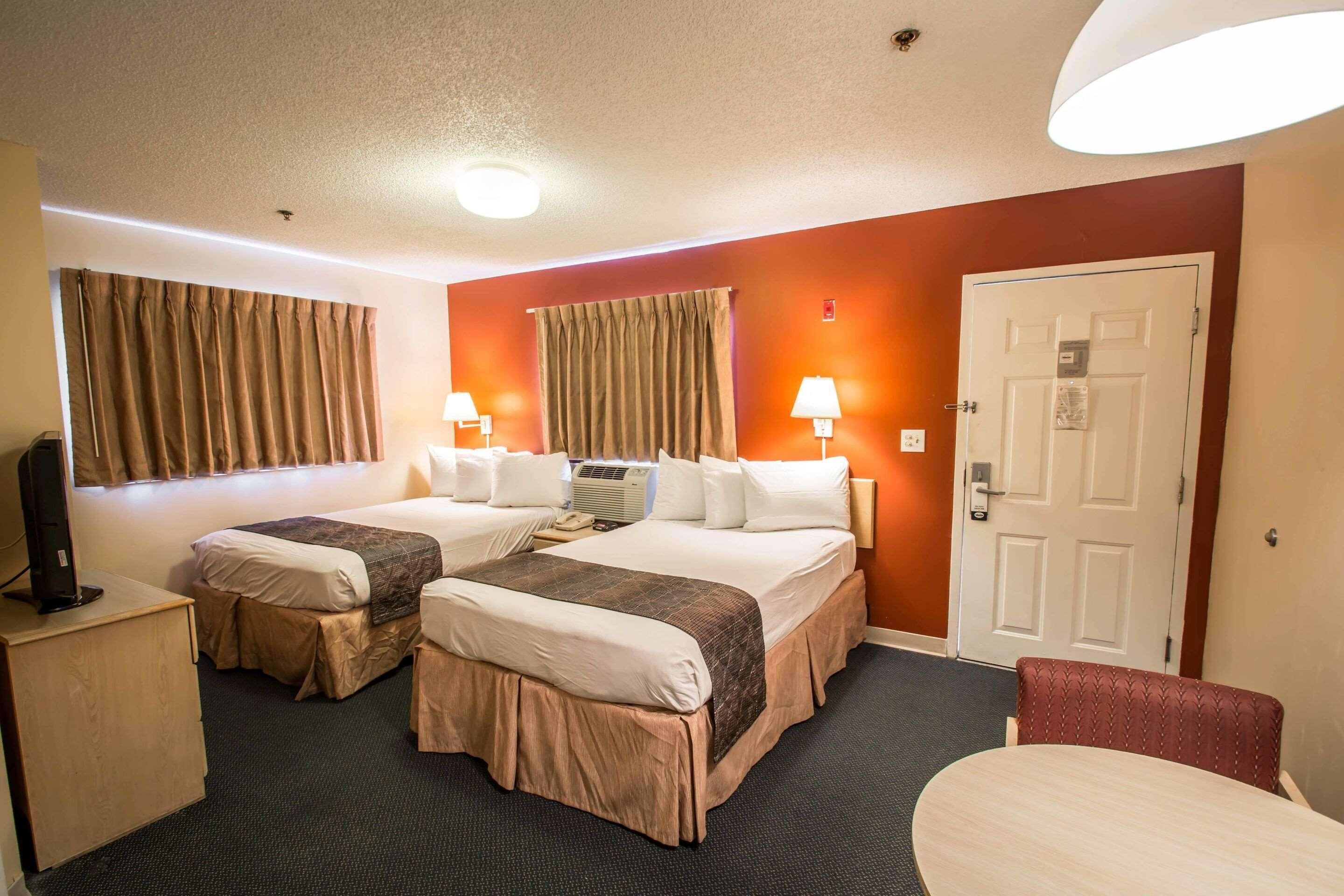 A hotel room with two beds, a desk, a chair, and a door.