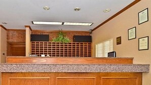 A reception desk with a wooden finish, a plant, and framed certificates on the wall. - Suburban Studios Stuart Near Federal Hwy 1 (Stuart)