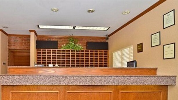 A reception desk with a wooden finish, a plant, and framed certificates on the wall. - Suburban Studios Stuart Near Federal Hwy 1 (Stuart)