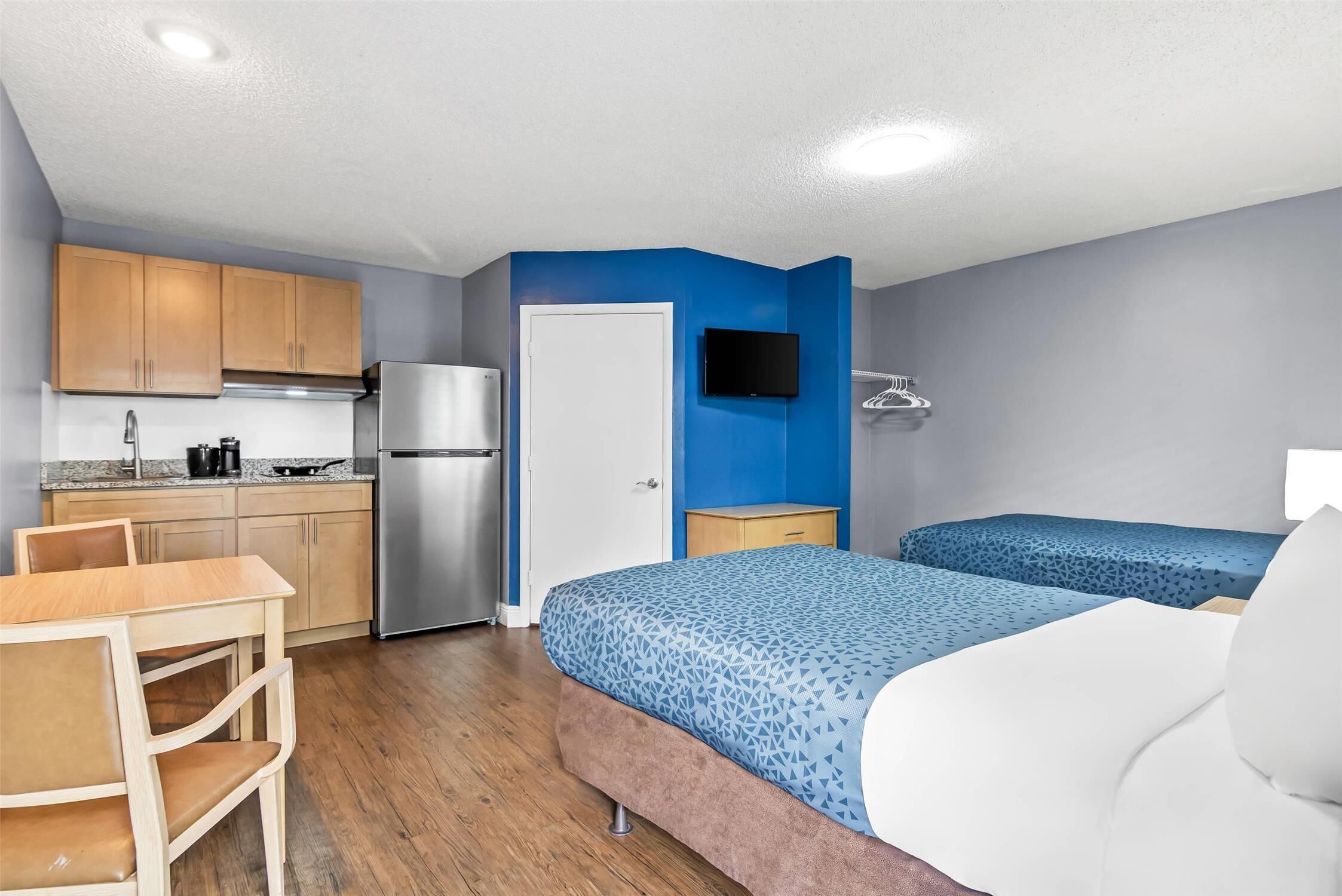 Una habitación compacta con kitchenette, una cama con ropa de cama estampada, un televisor montado en la pared y una silla de madera.