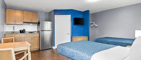 Una habitación compacta con kitchenette, una cama con ropa de cama estampada, un televisor montado en la pared y una silla de madera.
