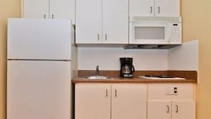 A compact kitchen with white cabinets, a microwave, and a coffee maker on the countertop. - Suburban Studios Stuart Near Federal Hwy 1 (Stuart)