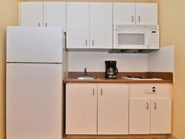 Cocina compacta con gabinetes blancos, microondas y cafetera sobre la encimera.
