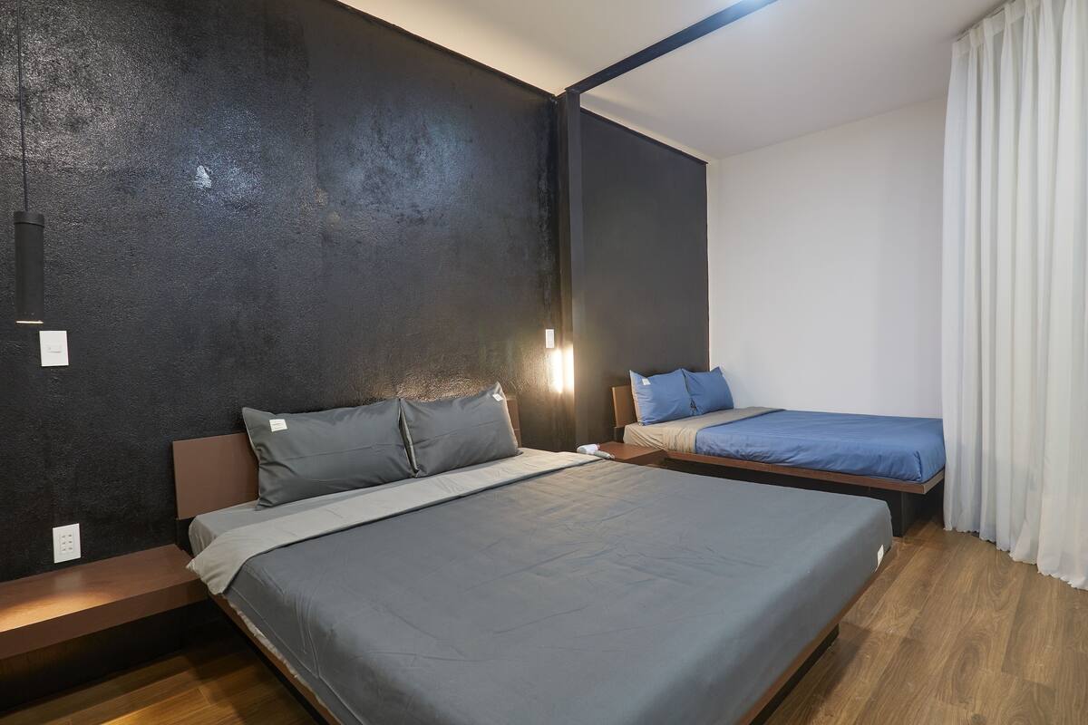 A modern hotel room with a large bed, a smaller bed, and a bench.