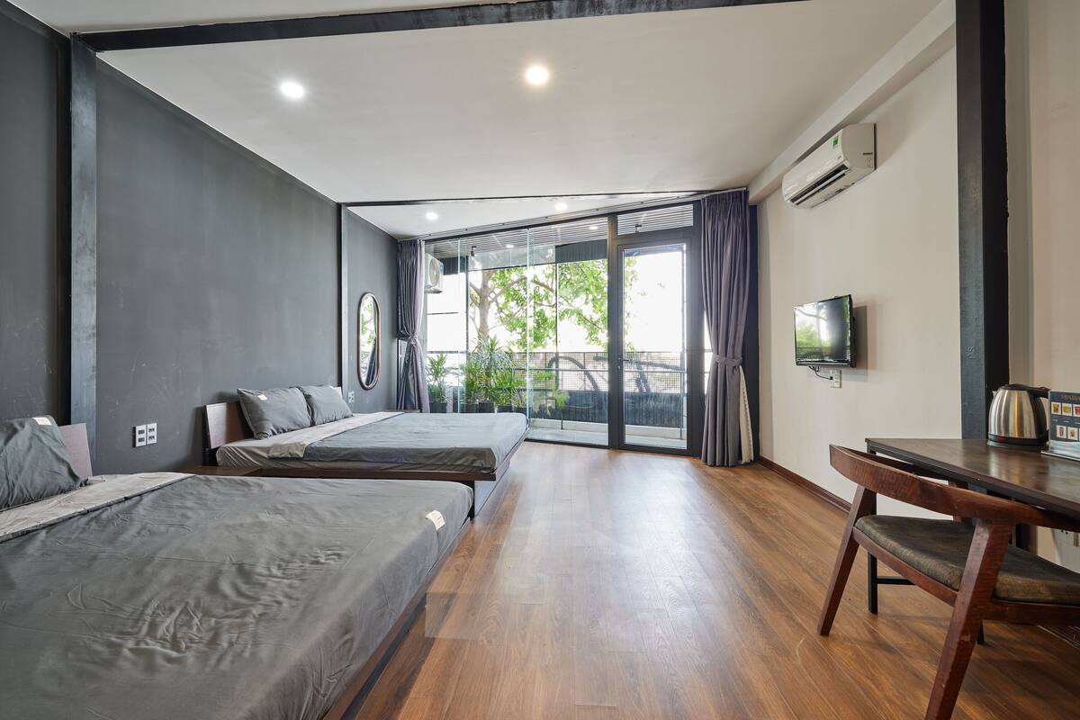 A modern hotel room with two beds, a wooden floor, a TV, and a balcony with curtains.
