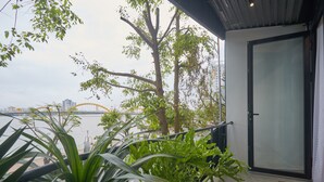 A balcony with potted plants, a glass door, and a view of a bridge and buildings across the water. - The Garden Capsule Hotel (Da Nang)