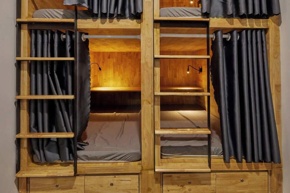 A wooden bunk bed room with curtains, a ladder, and a small desk.