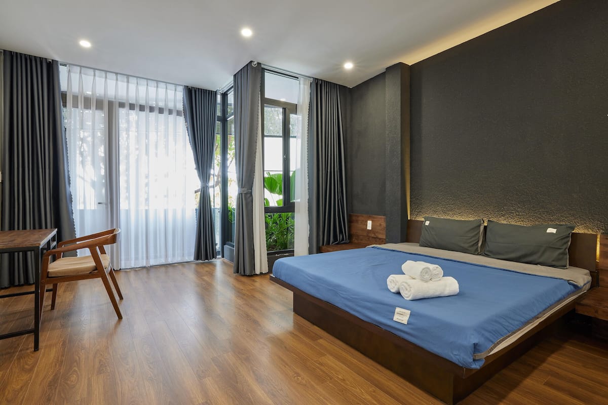 A modern hotel room with a wooden floor, a large bed with blue bedding, a wooden desk, and a chair.