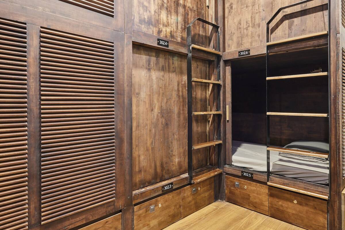 A compact, wooden room with built-in shelves and a ladder, featuring a bunk bed and a small desk area.