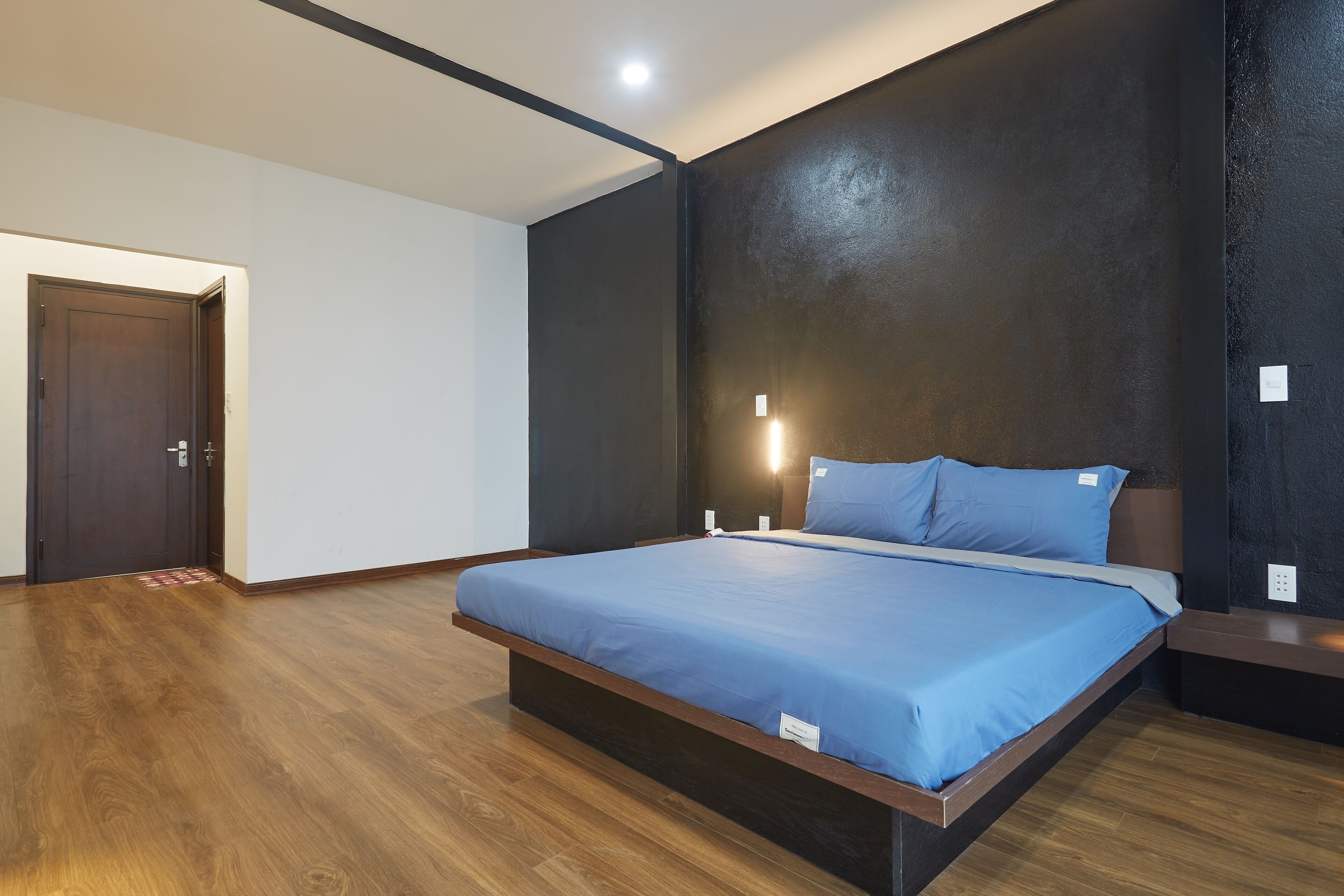 A modern bedroom with a large bed, wooden flooring, and a dark accent wall.
