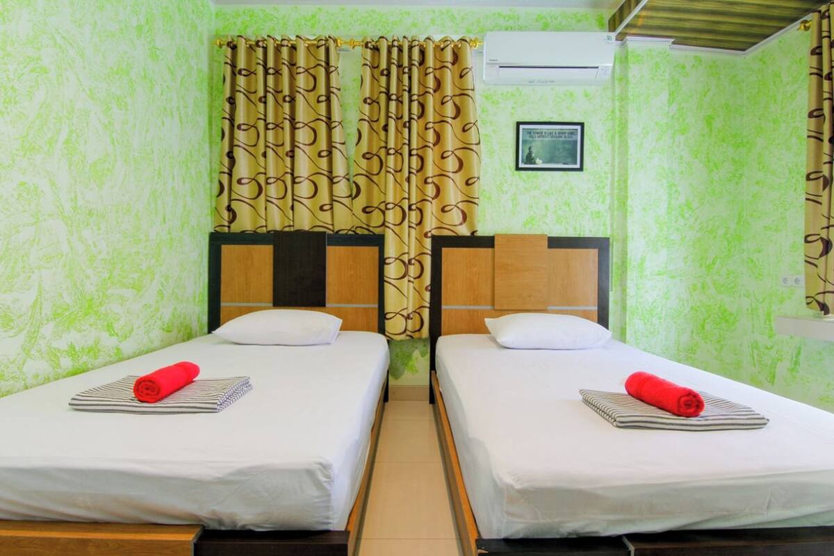 A room with two beds, a curtain, an air conditioning unit, and a framed picture on the wall.