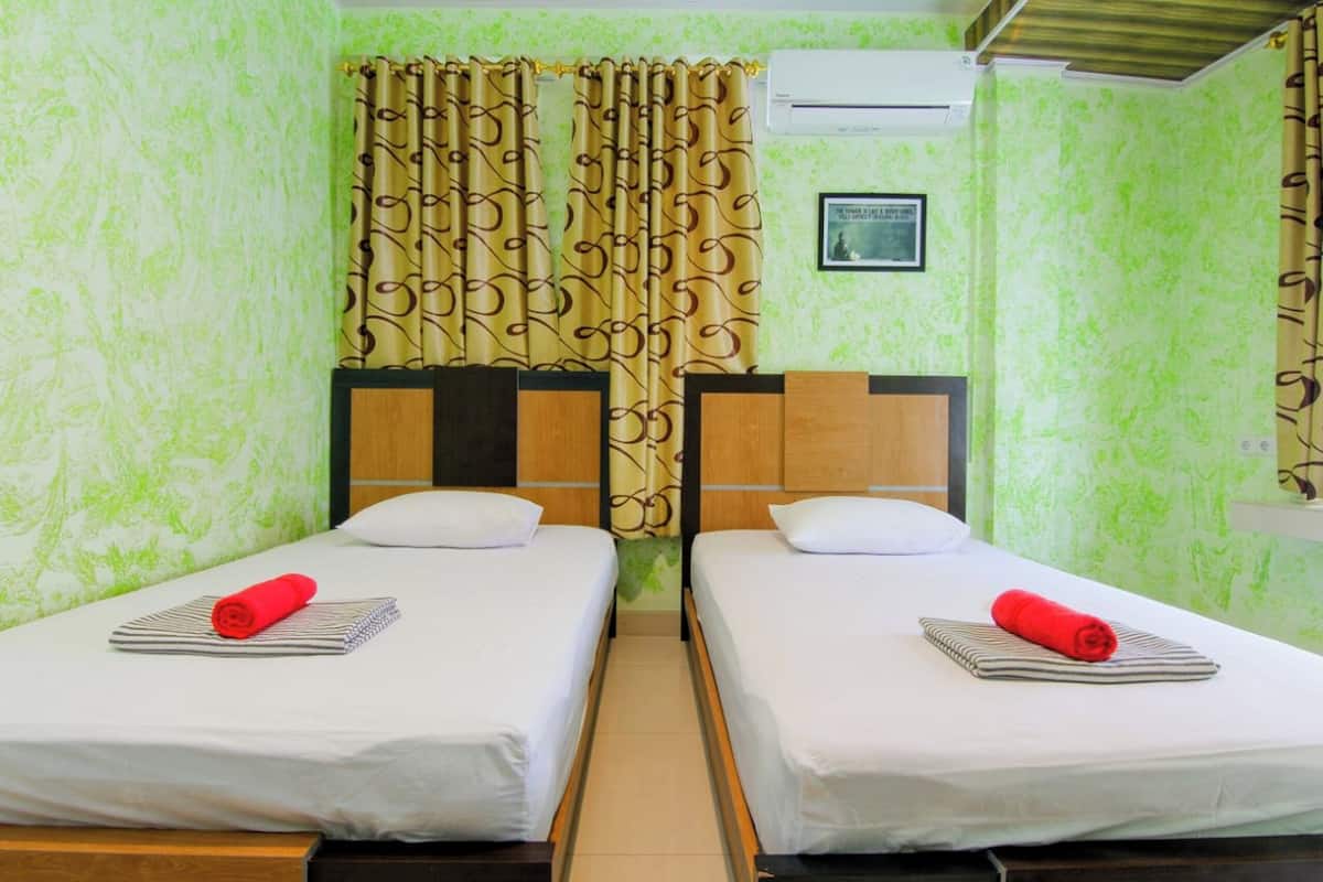 A room with two beds, a curtain, an air conditioning unit, and a framed picture on the wall.