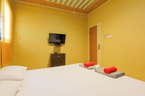 A hotel room with a bed, a television, a wooden cabinet, and a door. - Yani Homestay by Zuzu (Padang)