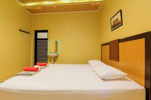 A hotel room with a bed, a sink, a mirror, and a coat rack. - Yani Homestay by Zuzu (Padang)