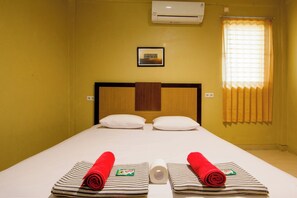 A hotel room with a bed, pillows, a rolled towel, a small framed picture, and an air conditioning unit. - Yani Homestay by Zuzu (Padang)