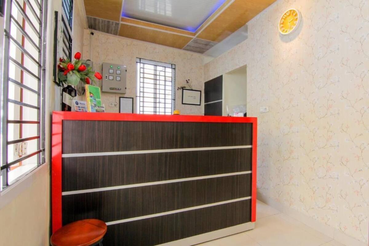 A reception desk with a red top, a window with bars, a wall clock, and a small plant.