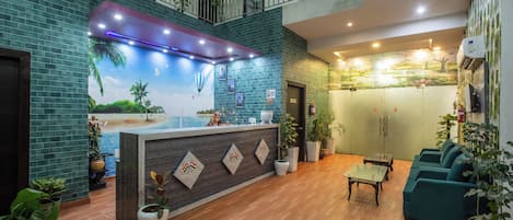 A hotel lobby with a reception desk, seating area, and a mural of a beach scene.