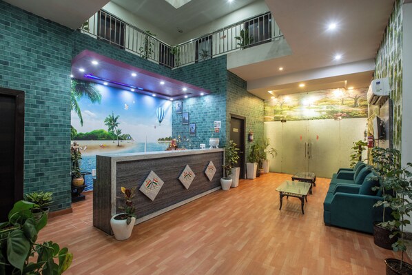 A hotel lobby with a reception desk, seating area, and a mural of a beach scene. - Hotel Sky View (New Delhi)