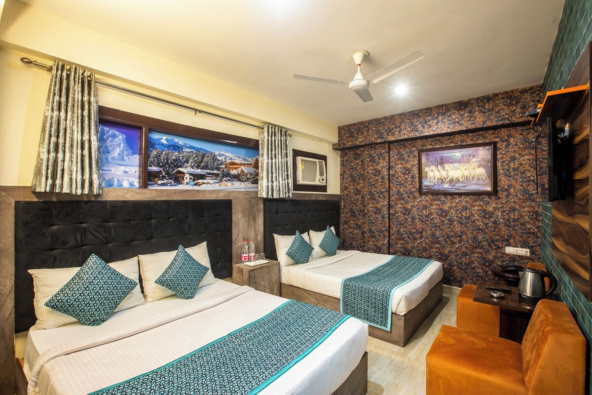 Habitación de hotel con dos camas, ventilador de techo, televisor montado y cafetera.