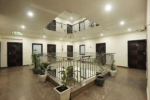 A multi-level atrium with a central staircase, potted plants, and a fire exit sign. - Hotel Sky View (New Delhi)