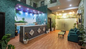 Un hall d’hôtel comprenant un comptoir d’accueil, un espace salon et une fresque représentant une scène de plage.