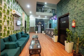 A lobby with green sofas, a glass-top table, potted plants, a fire extinguisher, and a conference hall door. - Hotel Sky View (New Delhi)