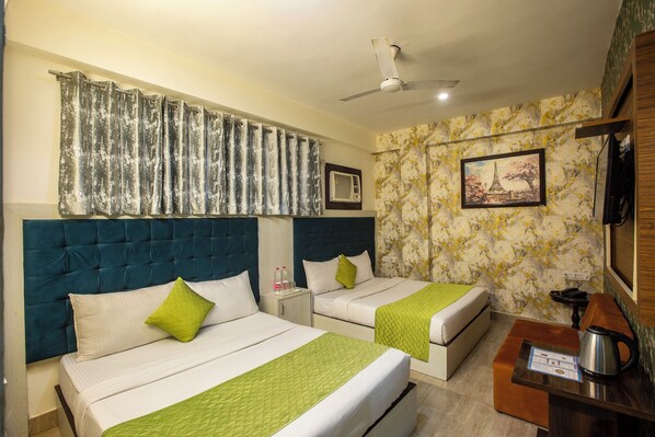 A hotel room with two beds, a ceiling fan, a painting, and a small table with a kettle. - Hotel Sky View (New Delhi)