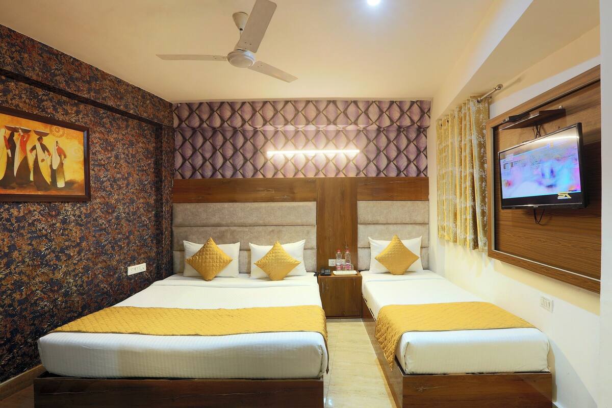 A hotel room with two beds, a ceiling fan, a TV, and a patterned wall.